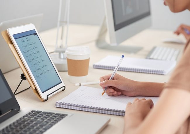 Student copying data from tablet computer to textbook during English class